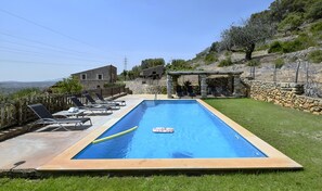 A rectangular swimming pool with a stone border, surrounded by lounge chairs and a stone wall. - Stunning Finca with Heated Pool for 8 Guests (Illes Balears)