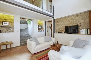 A modern living room with two white sofas, a flat-screen TV, and a stone wall. - Stunning Finca with Heated Pool for 8 Guests (Illes Balears)
