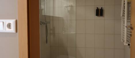 A bathroom with a shower, toilet, and two bottles of shampoo on the wall.