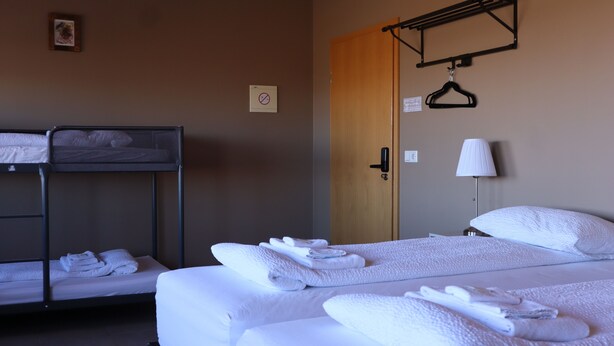 A hotel room with bunk beds, a wooden door, a towel rack, and a lamp. - Blue Viking Studios (Reykjanesbær)