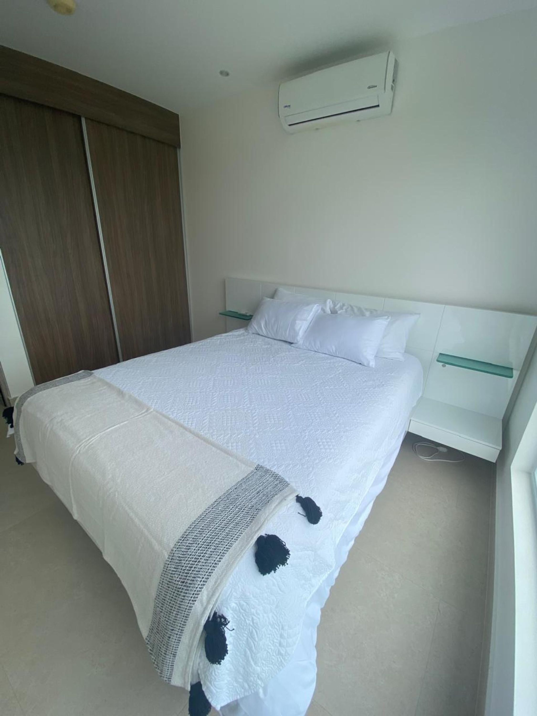 A hotel room with a large bed, a bedside table, a wardrobe, and an air conditioning unit on the wall.