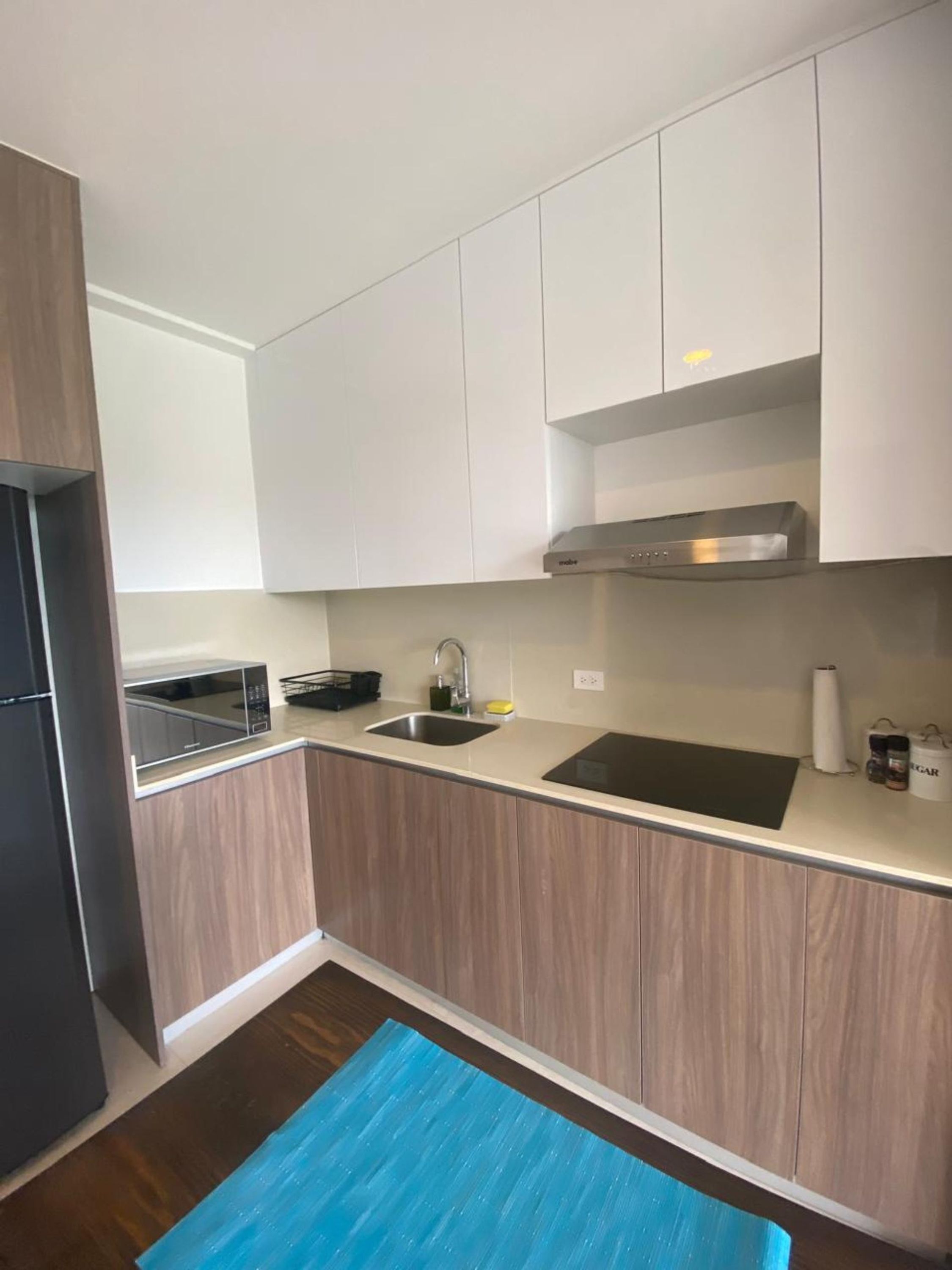Una cucina moderna con mobili bianchi, un lavello in acciaio inossidabile e un forno a microonde.