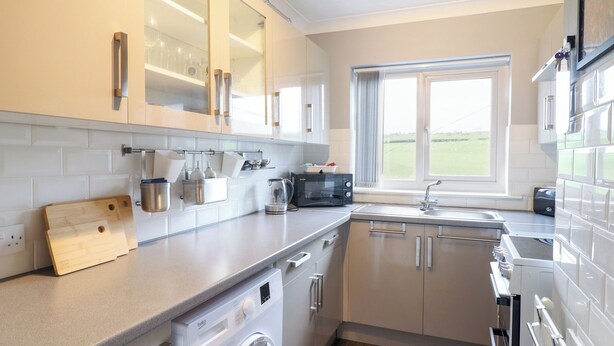 A modern kitchen with a built-in washing machine, a microwave, and a window with a view of the outdoors. - Golygfa (Abergele)
