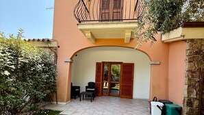 A two-story building with a balcony, a stone wall, and a small patio area with outdoor seating. - Casa Vacanza Gallura in Centro (San Teodoro)