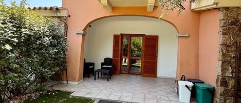 Un edificio de dos pisos con un balcón, una pared de piedra y un pequeño patio con mobiliario exterior.