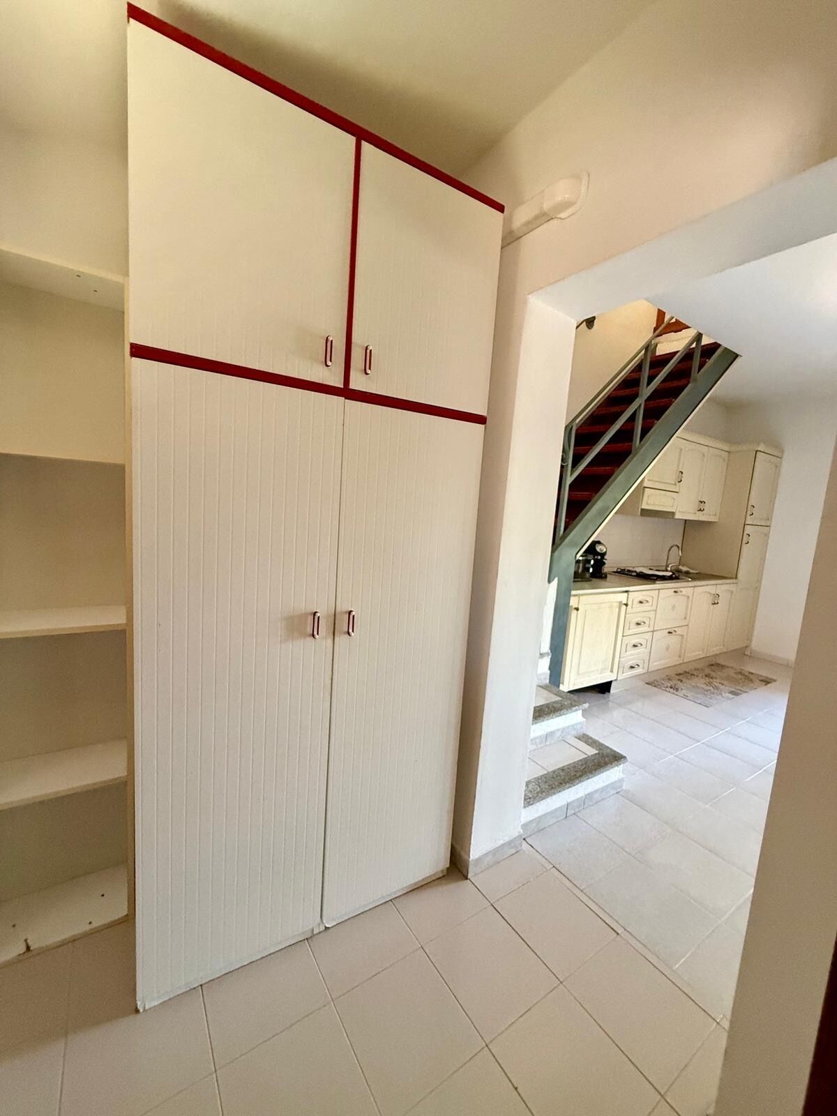 A room with a wardrobe, a staircase, and a kitchen area.