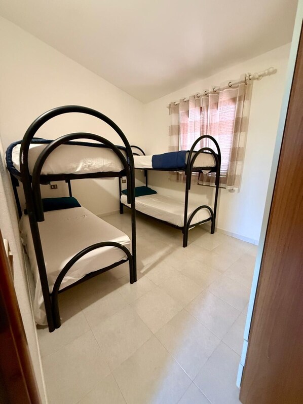 A room with three bunk beds, a window with curtains, and a tiled floor. - Casa Vacanza Gallura in Centro (San Teodoro)