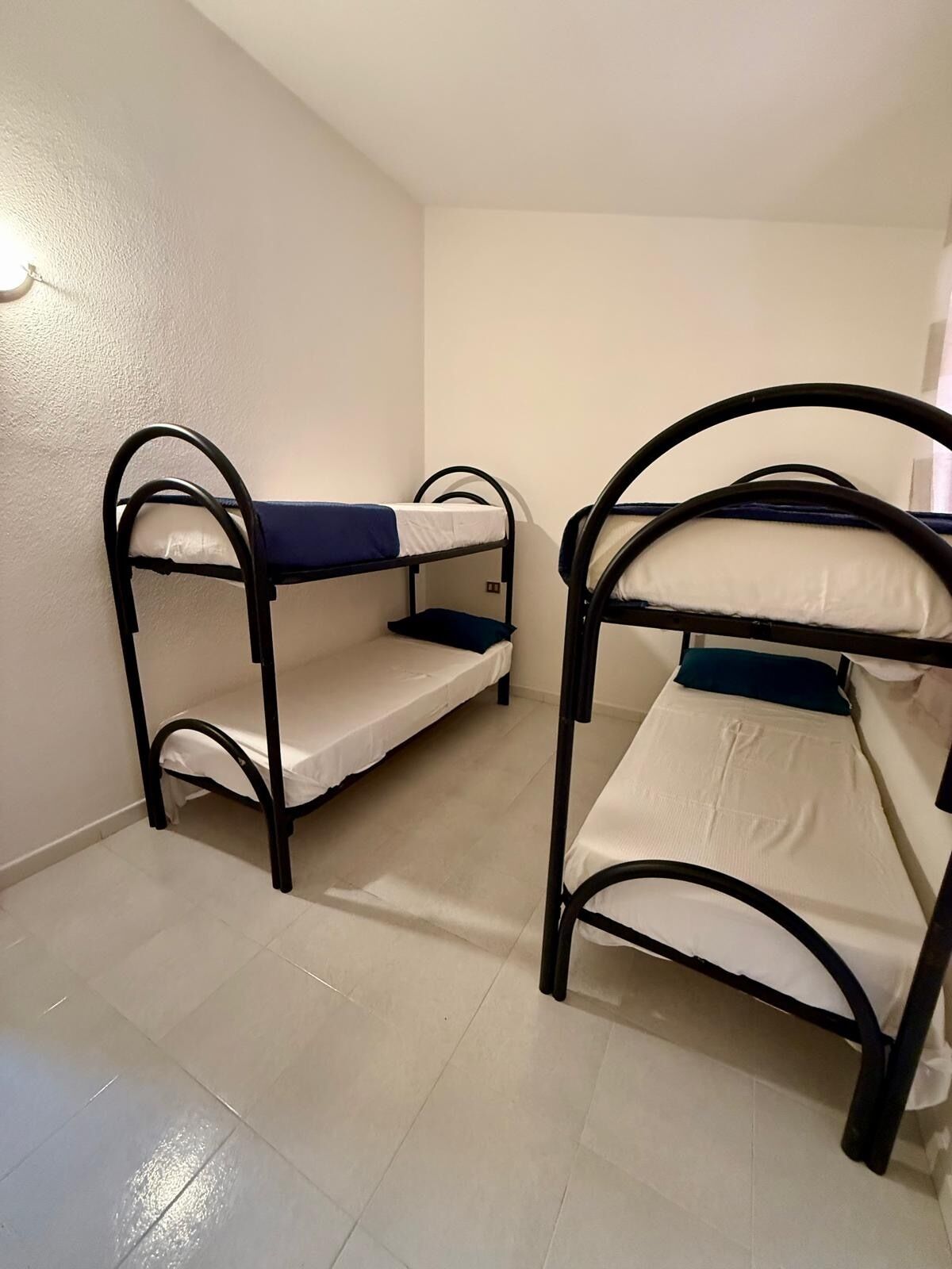 Two bunk beds in a room with white walls and tiled flooring.