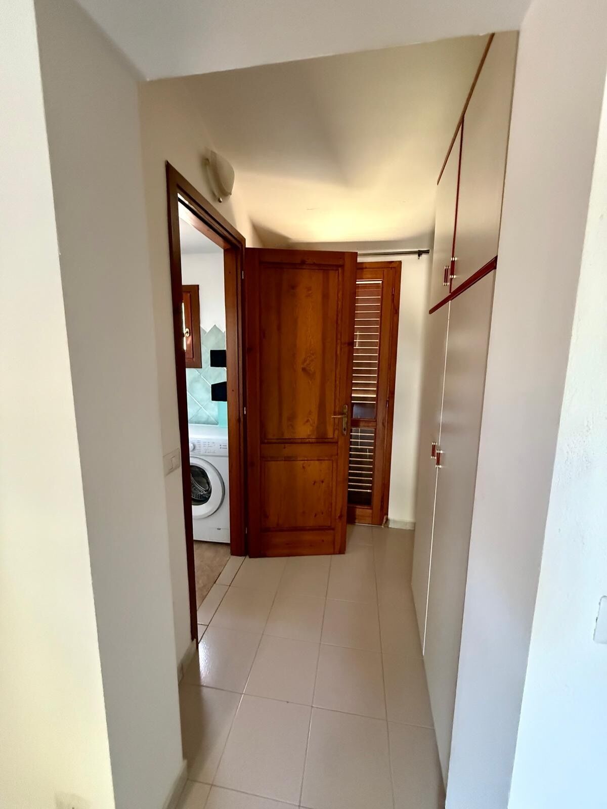 A narrow hallway with a wooden door, a laundry area with a washing machine, and a closet with sliding doors.