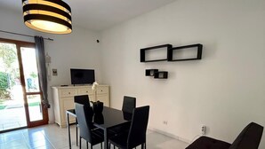 A modern living room with a dining area, a sofa, a TV, and a ceiling light fixture. - Casa Vacanza Gallura in Centro (San Teodoro)