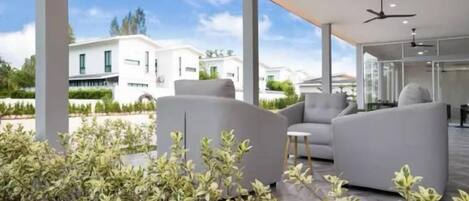 A modern outdoor seating area with a white sofa and a small table, surrounded by greenery.