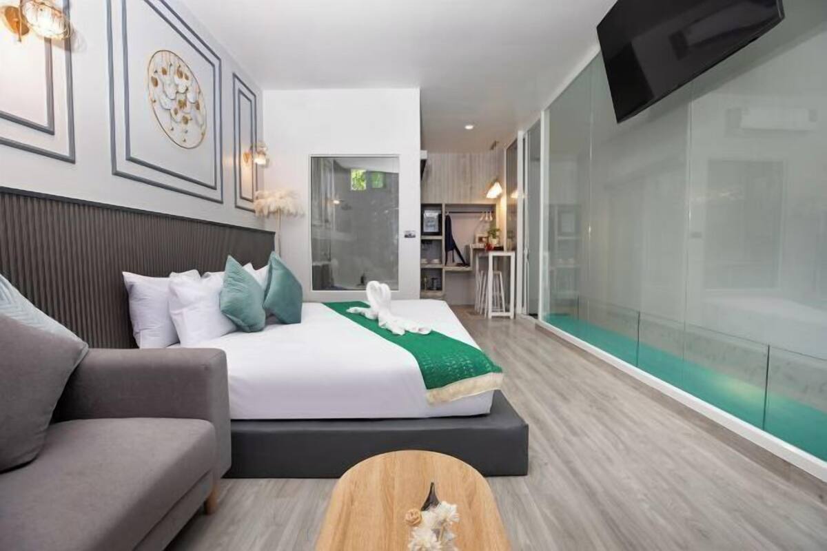Een moderne hotelkamer met een bed, een bank, een televisie en een glazen wand.