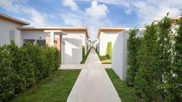 A pathway leading to a row of white buildings with orange roofs, surrounded by green hedges.