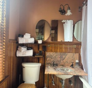 Ein kleines Badezimmer mit Waschtisch aus Holz, Toilette, Spüle mit Marmorplatte und Spiegel über der Spüle.