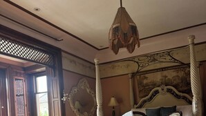Une chambre à coucher avec un lit à baldaquin, un lustre et une vue sur l’extérieur par une fenêtre.