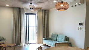 A modern living room with a round wooden dining table, two sofas, and a ceiling fan. - An Corner - Sora Garden II Apartment (Ho Chi Minh City)