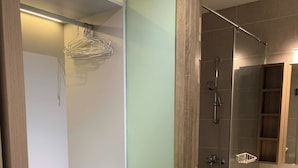 A modern bathroom with a glass-enclosed shower, a wooden vanity, and a white shelf. - An Corner - Sora Garden II Apartment (Ho Chi Minh City)