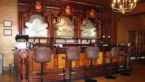 Zona de bar con mostrador de madera, taburetes y una lámpara de araña.
