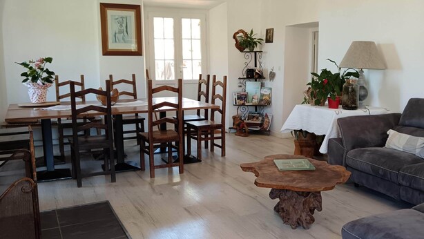Een eetgedeelte met houten stoelen en een tafel, een woonkamer met een bank en salontafel, en een boekenkast met diverse objecten.