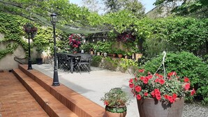 Een terras met een tafel en stoelen, omringd door plantenpotten en een bakstenen muur.