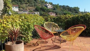Een terras met twee rieten stoelen en een grote potplant.