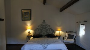 Een slaapkamer met een groot bed, twee bedlampen, een stoel en een ingelijst schilderij aan de muur.