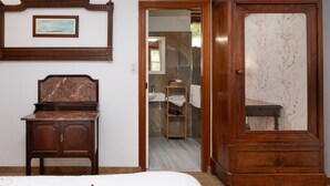 A bedroom with a bed, a wooden dresser, a mirror, and a bathroom visible through an open door.