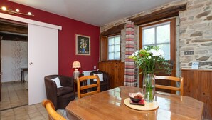 A dining area with a wooden table, chairs, a vase with flowers, and a red wall with a painting.