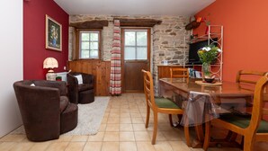 A cozy living room with a fireplace, a dining area with a table and chairs, and a kitchen area with a TV and a fruit bowl.