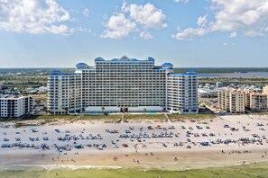 Ein großes Hotel mit mehreren Etagen und einem Strand im Vordergrund.