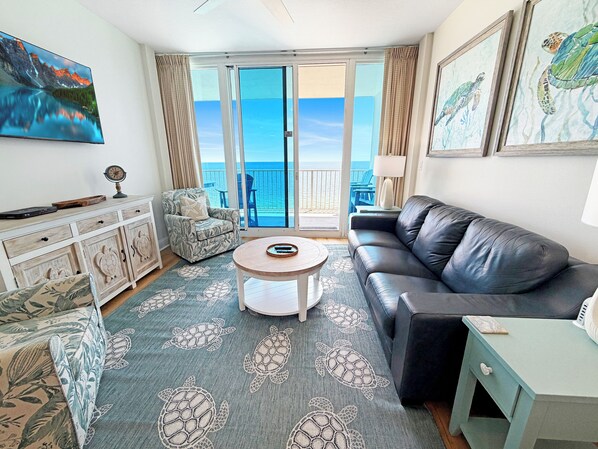 Ein Wohnzimmer mit Sofa, Sessel, Couchtisch und Meerblick durch große Glasfenster.