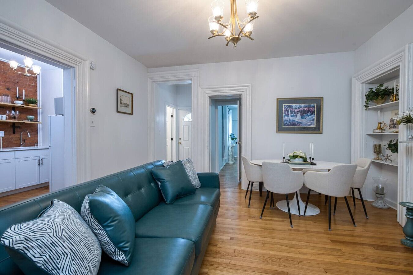 Un salon moderne avec un canapé de couleur turquoise, un coin repas avec des chaises blanches et une cuisine avec des meubles blancs.