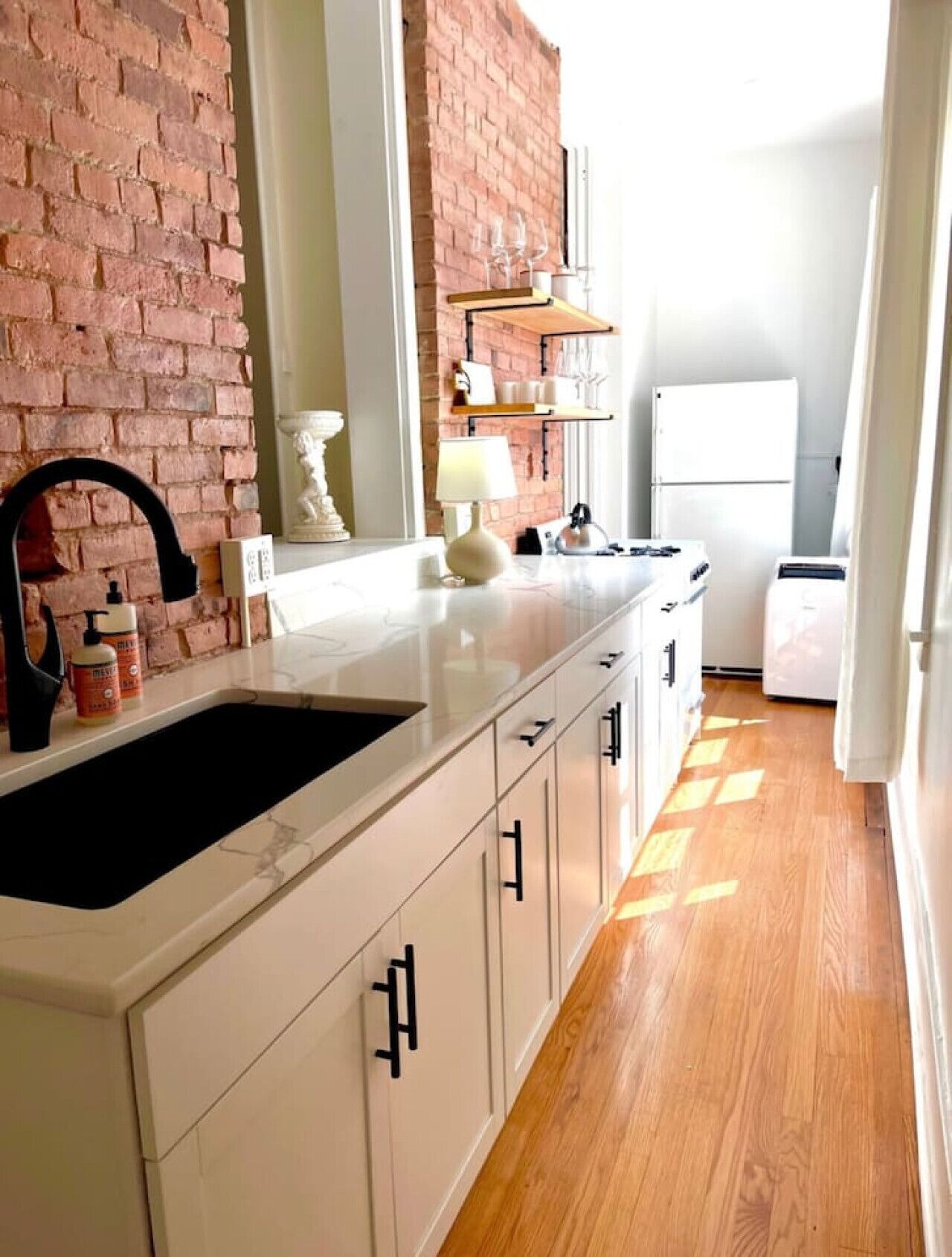 A kitchen with a brick wall, white cabinets, a black faucet, and a white refrigerator.