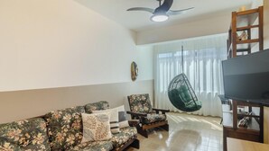 A living room with a sofa, chairs, a hanging chair, a TV, and a ceiling fan.
