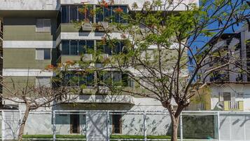 Un edificio residencial de varios pisos con balcones, un árbol en primer plano y cielo despejado.