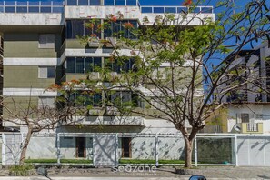 Ein mehrstöckiges Wohnhaus mit Balkonen, ein Baum im Vordergrund und ein klarer Himmel.