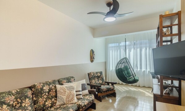Ein Wohnzimmer mit einer Couch, Sesseln, einem Hängesessel, einem Fernseher und einem Deckenventilator.
