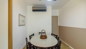 A dining area with a round table, chairs, a ceiling fan, an air conditioning unit, and a framed picture on the wall.