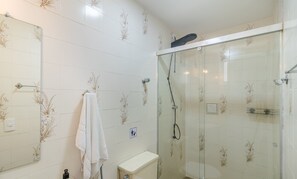Een badkamer met een douchecabine van glas, een wit toilet en een handdoek aan een rek.