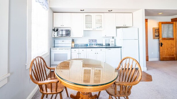 A modern kitchen with white cabinets, a glass-top dining table, and wooden chairs.