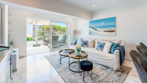 A modern living room with a white sofa, a coffee table, and a painting of a beach scene. - Casa Aurora - Vale do Lobo (Vale do Lobo)