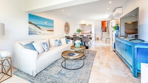A modern living room with a white sofa, a coffee table, and a painting of a beach scene. - Casa Aurora - Vale do Lobo (Vale do Lobo)