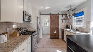 A modern kitchen with white cabinets, stainless steel appliances, and a large wooden door. - Charming Craftsman in Downtown SJ (San Jose)