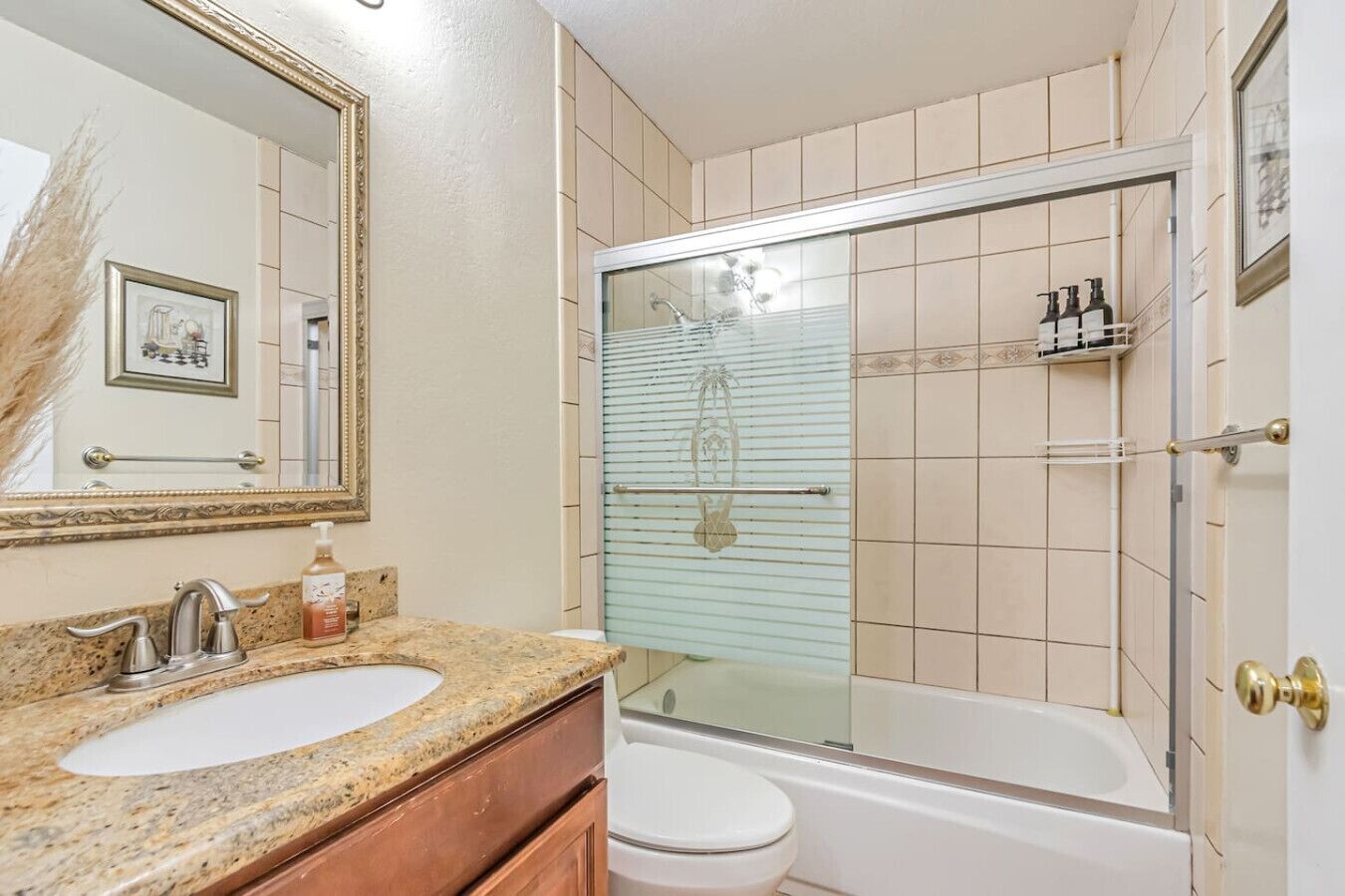 A bathroom with a granite countertop sink, a toilet, a glass-enclosed shower, and a mirror with a decorative frame.