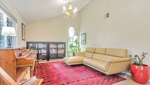 A spacious living room with a piano, a beige sofa, a red patterned rug, and a chandelier. - Tranquil 3BDR/2BA Fremont Escape (Fremont)