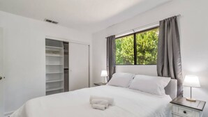 A bedroom with a bed, two bedside tables with lamps, a wardrobe, and a window with curtains.