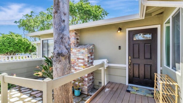 A house with a wooden deck, a brick fireplace, and a dark front door.