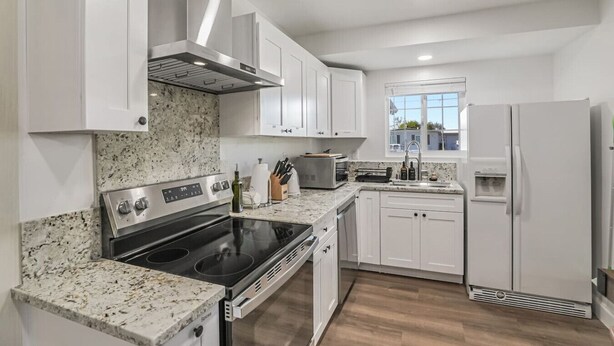 A modern kitchen with white cabinets, a stainless steel stove, a built-in oven, a microwave, and a refrigerator.