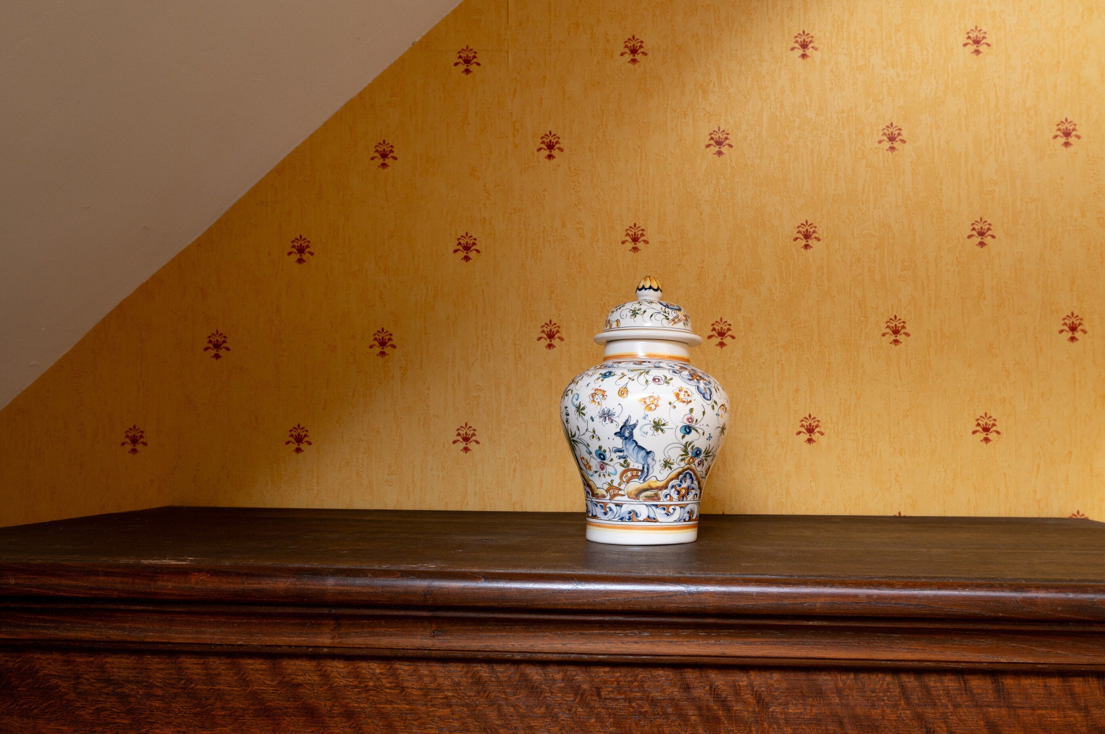 A ceramic vase on a wooden surface against a patterned wall.