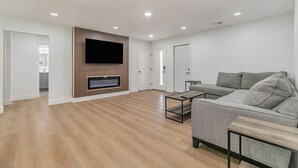Una sala de estar moderna con un sofá gris, un televisor de pantalla plana montado en un panel de madera y una mesita.